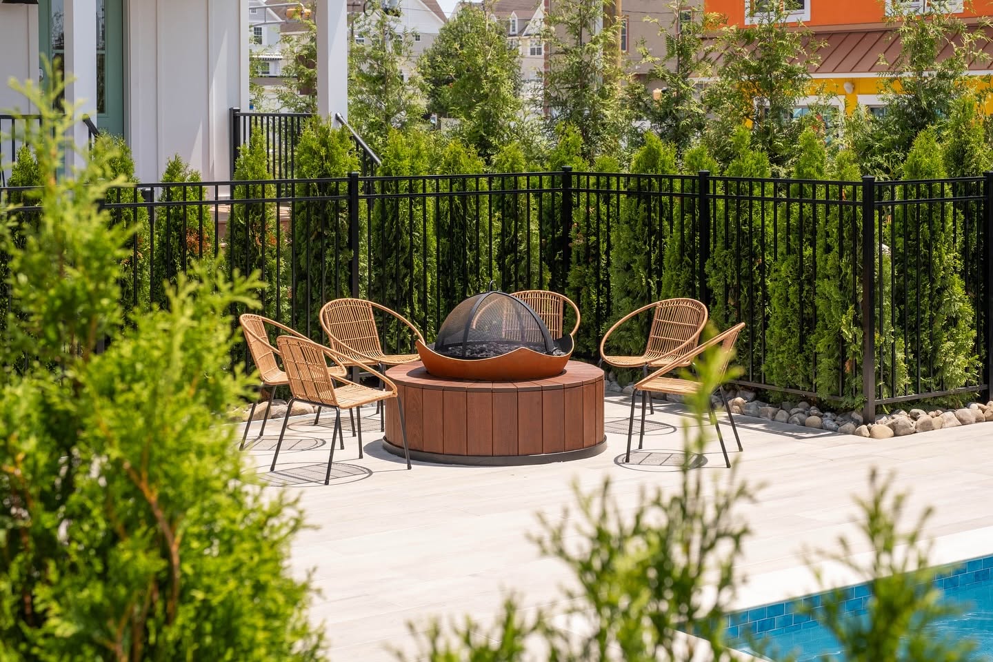 Poolside firepit lounge with woven chairs surrounded by greenery at The Hen Houses